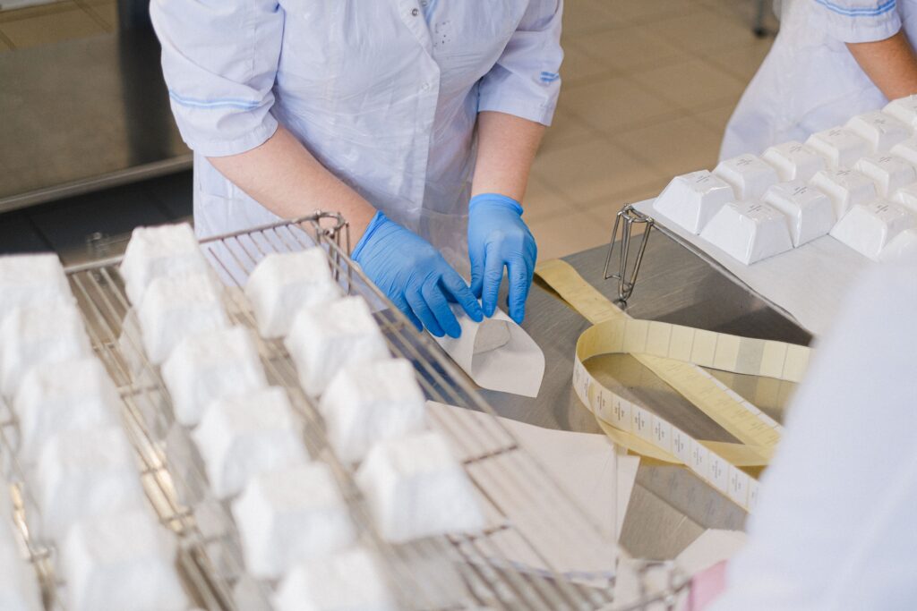 Close-up of hands in blue gloves wrapping cheese blocks in an indoor setting.